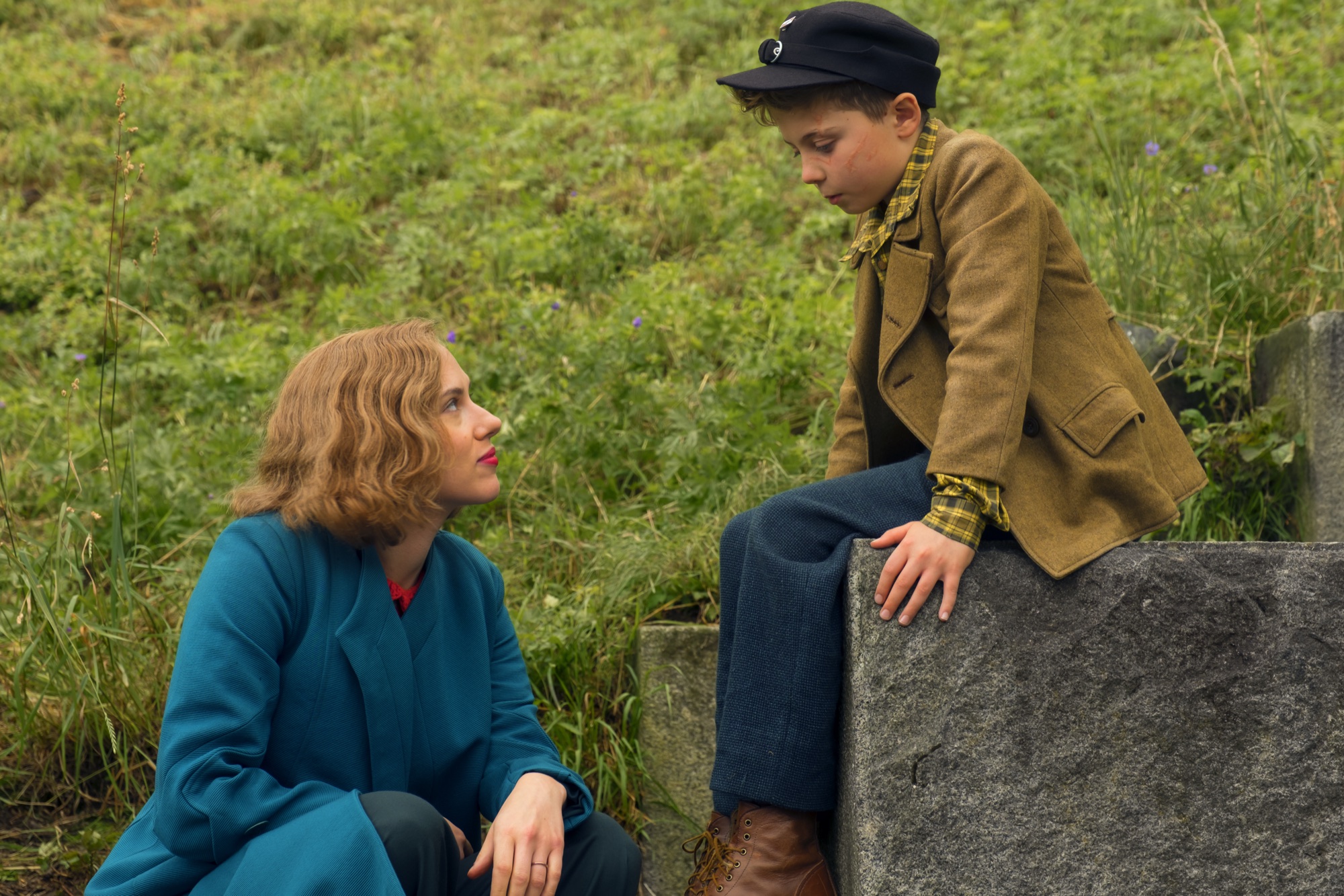 Rosie looking up at Jojo beside a stone wall in Jojo Rabbit
